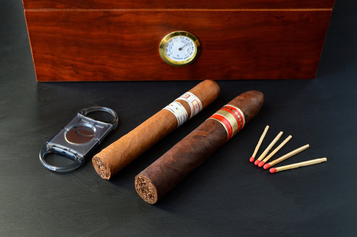 Cigars displayed in front of a wooden humidor with a cigar cutter